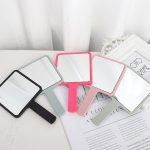 A square handheld mirror assortment in grey, pink, black, and light green. Each features a sleek design and a handle.