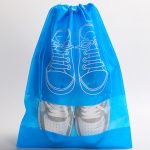 A blue non-woven drawstring bag with a clear window displaying a pair of white shoes inside. It features a shoe design.