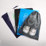 A collection of non-woven drawstring bags in various colours, featuring clear windows and shoe graphics.