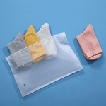 A matte frosted zip-lock storage bag containing grey, yellow, and white socks, with a pink sock placed beside it.
