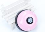 A pink pet training bell with a black centre, featuring paw print designs, placed on a white wooden stand.