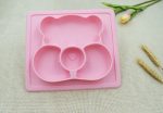 A pink non-slip children's plate featuring a bear design with three compartments, accompanied by a flower and decorative elements.