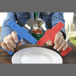 A blue airplane-shaped fork and a red airplane-shaped spoon held above a white plate. The cutlery features star designs.