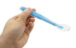 A baby training spoon in blue held by a hand, featuring a transparent tip and a logo on the handle.