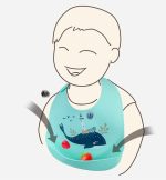 A silicone baby bib in light blue featuring a whale design, with a catch pocket for food. It has a branding logo.
