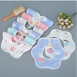 A collection of colourful baby saliva towels featuring various cute patterns, arranged neatly with a wooden brush and flowers.