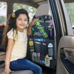 A car seat organiser bag featuring various compartments, drinks, pens, and toys. The bag is black with colourful items displayed.