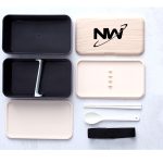 A double-layer lunch box set in black and cream, featuring a spoon, dividers, and a black strap. Includes a logo.