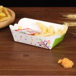 A food tray in green and white, featuring colourful dots and a floral design, filled with fries and a sauce packet.