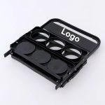 A black beer basket with four circular holders and a handle, featuring a logo on the front.