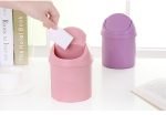 A pink and a purple mini trash can are displayed on a table, with a hand dropping a piece of paper into the pink one.
