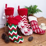 A collection of red and white Christmas stockings with various festive patterns, placed on a wooden surface surrounded by pine cones.