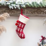 A red Christmas stocking with a white knitted cuff, featuring white snowflakes and red pom-poms, hanging decoratively.