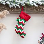 A Christmas stocking with a red top and a green, white, and red zigzag pattern, featuring a pom-pom.