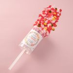 A clear drink bottle filled with red, pink, and yellow confetti, featuring a decorative label and straw.