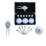 A golf set featuring three white golf balls, tees, a pitch fork, and a black case with a logo.
