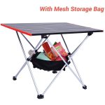 A portable camping table with a black top, red edges, and a mesh storage bag underneath filled with items.