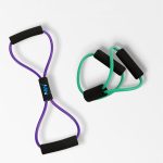 A purple yoga stretch band with black handles and two green resistance bands with black handles.