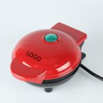 A red heart-shaped baking waffle maker with a green indicator light and a black base, featuring a logo.