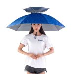 A blue folding sun and rain umbrella cap held by a person wearing a white T-shirt and shorts.