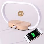 A wooden bedside lamp with a white curved light, featuring a wireless charging pad and a smartphone charging indicator.