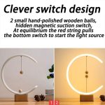 A decorative lamp featuring a curved white frame, wooden balls, and a warm light source, set on a wooden base.