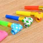 A collection of brightly coloured party whistles in various patterns, including polka dots and checkers, on a wooden surface.