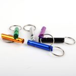 A set of portable aluminium whistles in orange, silver, purple, green, black, and blue, attached to keyrings.