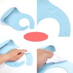 A light blue silicone baby bib with a hand wiping it clean, featuring a logo. Water droplets are visible on the bib.