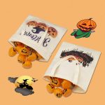A reusable canvas tote bag in cream with a logo, filled with orange Halloween-themed items.