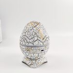 A cracked white and gold egg-shaped projector with buttons at the base sits on a flat surface.