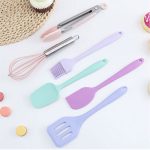A six-piece baking tool set featuring pastel colours, including a whisk, spatula, and tongs, with a branding logo.