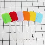 A set of six cream spatulas in vibrant colours: green, red, purple, orange, yellow, and blue, with clear handles.