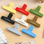 A set of eight magnetic plastic clips in various colours: yellow, red, black, white, grey, green, brown, and blue. Each has a logo.