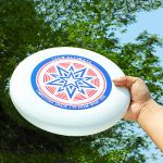 A white Ultimate Disc Frisbee held in a hand, featuring a colourful star design and a logo.