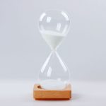 A five-minute sand timer with a wooden base and transparent glass hourglass. White sand is visible inside.