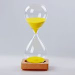 A clear glass sand timer with yellow sand, set on a wooden base.