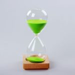 A sand timer with a wooden base and bright green sand, featuring a classic hourglass shape.
