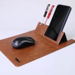 A brown mouse pad with a pen holder and a smartphone stand, accompanied by a black mouse and two pens.