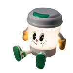 A light-up, coffee cup-shaped lamp features a friendly face with green accents and a base resembling a speaker.