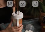A drink bottle with a compartmentalised design, featuring a double straw and a white lid. It has a logo.
