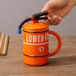 A drink mug in the shape of a fire extinguisher, featuring an orange body and a black handle with a nozzle.