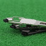 A multi-functional 7-in-1 golf tool in silver and black on a green turf background, featuring various brushes and tools.