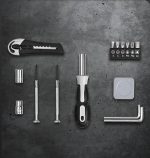A set of metallic and black tools, including screwdrivers, a utility knife, and various bits on a textured surface.