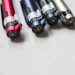A collection of four multi-tool pens in red, navy, silver, and black, each featuring a compass on the end.