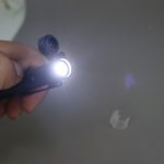 A black multi-tool pen with an LED light at the tip, being held in a hand.
