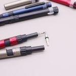 A collection of 6-in-1 multi-tool pens in red, black, blue, and gold, featuring various tips and a logo.