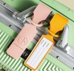 A pink and yellow leather luggage tag attached to a green suitcase, featuring a logo and space for personal information.