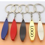 A surfboard-shaped keychain in blue, red, black, gold, and silver, attached to keyring chains.