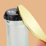 A sleek gold bottle opener with a curved design, held above a black bottle cap.